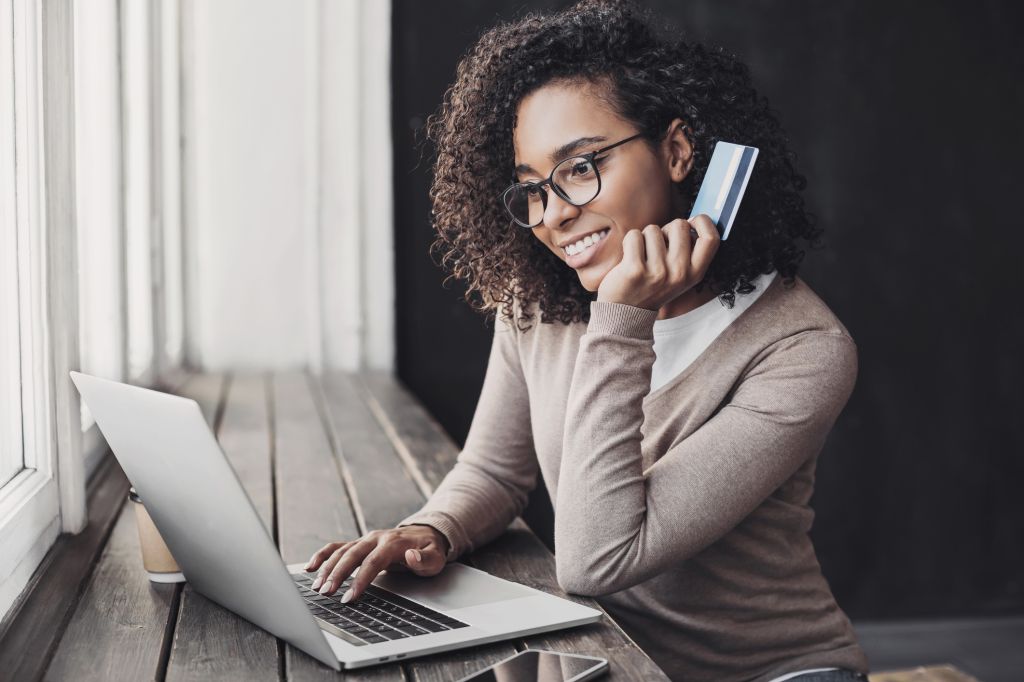 A smiling woman holding her credit card while using her laptop