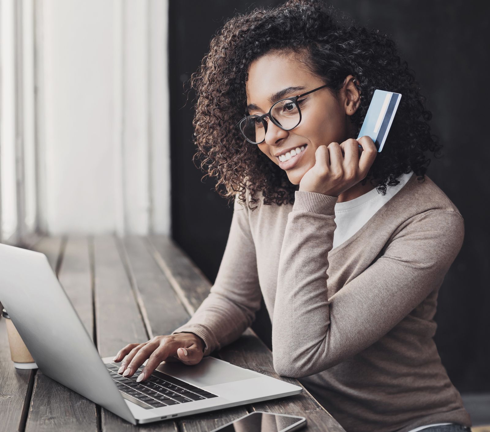A smiling woman holding her credit card while using her laptop