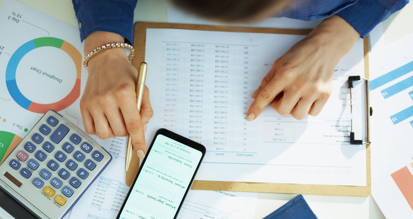 A woman using her phone and a calculator while reading through documents