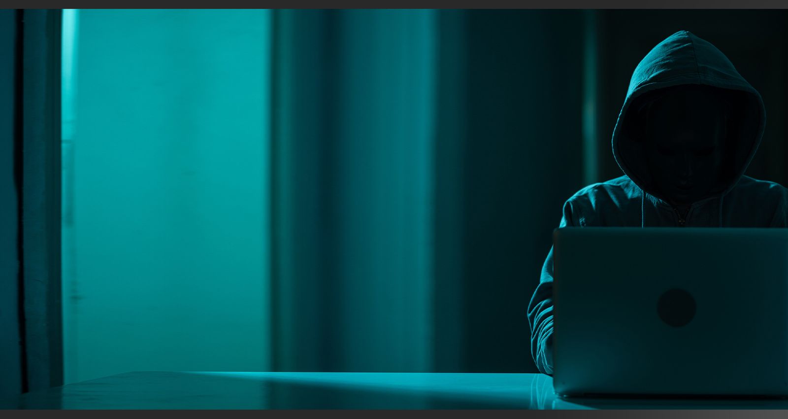 Man wearing a hood hacking a computer in a dark room