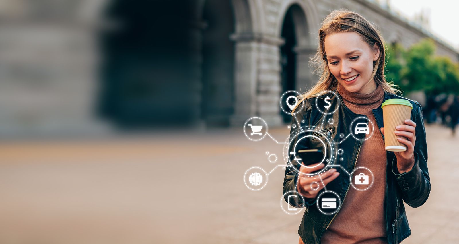 Woman smiling outside while drinking coffee and looking down at her phone