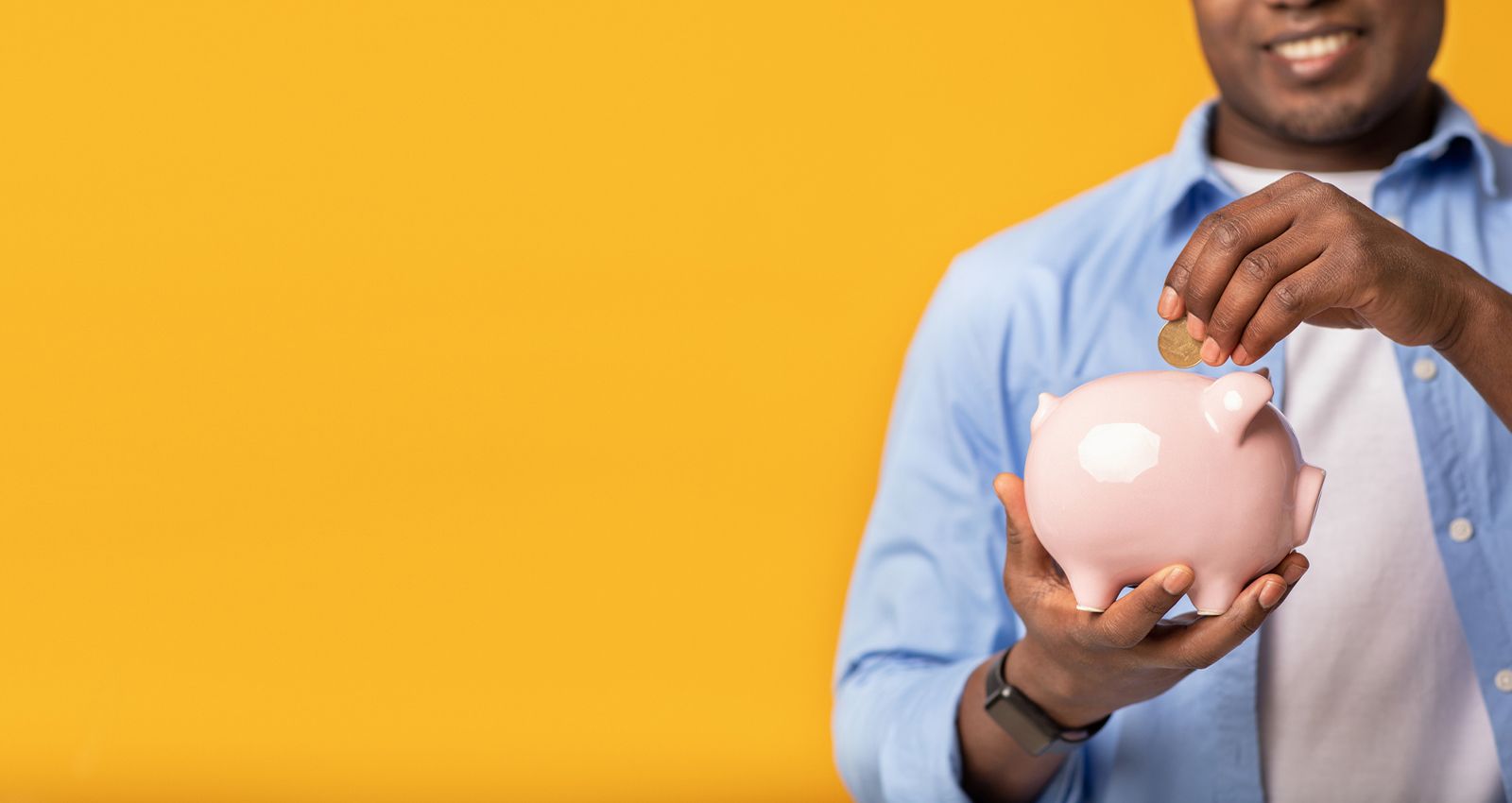 A smiling man putting money into a piggy bank