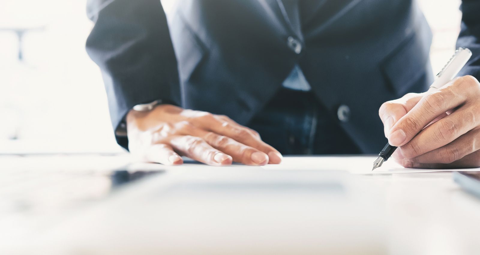 A man in a suit taking notes while leaning over a desk