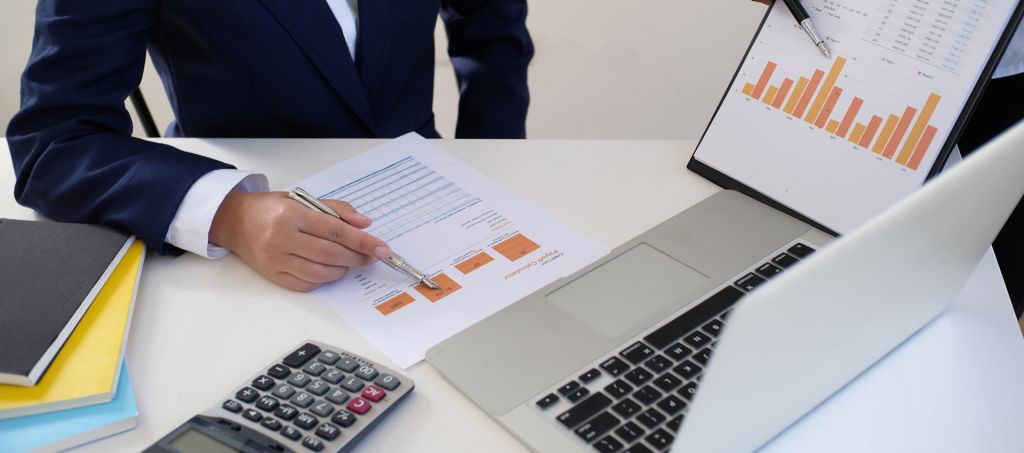 Man at a table looking through charts in front of his laptop