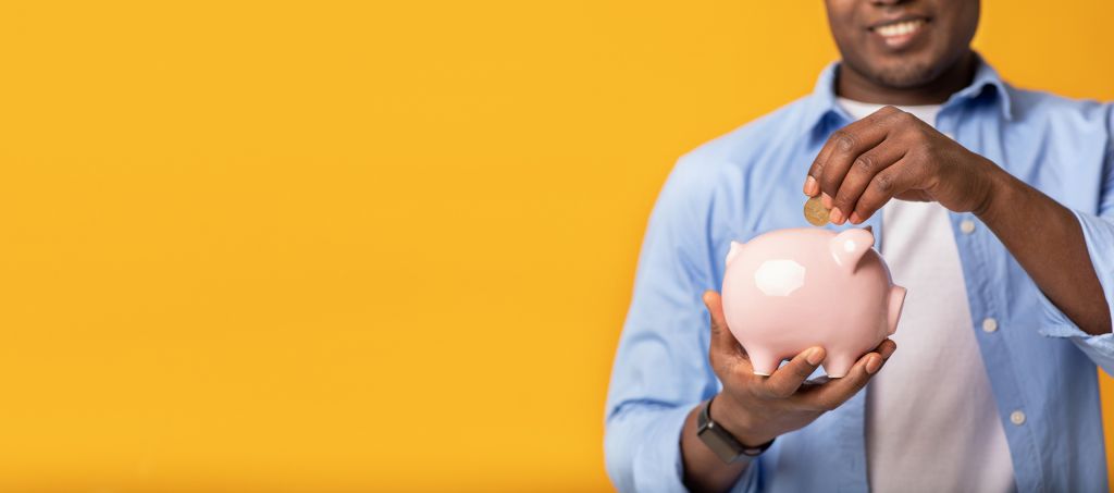 A smiling man putting money into a piggy bank