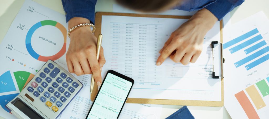 A woman using her phone and a calculator while reading through documents