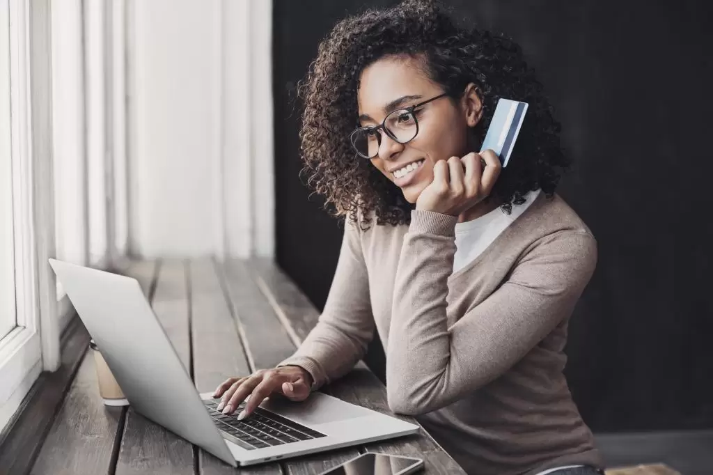 A smiling woman holding her credit card while using her laptop
