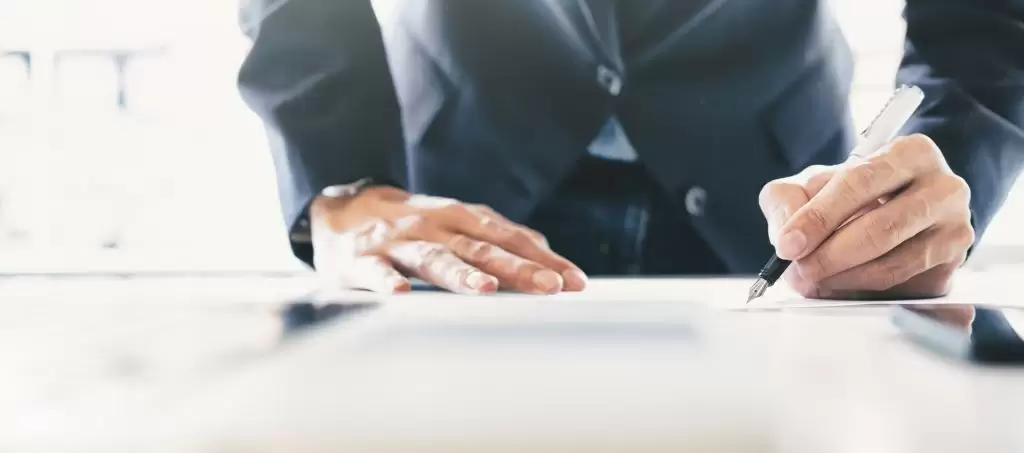 A man in a suit taking notes while leaning over a desk